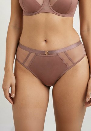Kobieta ubrana w majtki z przezroczystymi panelami w kolorze mauve z wysokim stanem i dopasowany biustonosz, stojąca z ramionami swobodnie opadającymi wzdłuż boków na jednolitym tle.