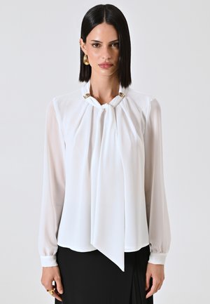 Blusa bianca realizzata in tessuto leggero con un design drappeggiato, dotata di dettagli in metallo dorato al collo, maniche lunghe e un pannello anteriore morbido.