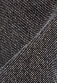 Gros plan sur un tissu en denim gris foncé montrant une texture de tissage diagonal détaillée et un pli.