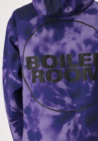 Purple tie-dye hoodie featuring a large black "BOILER ROOM" logo within a circular outline on the back. Material appears smooth with a relaxed fit.
