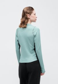 Hosszú ujjú felső menta zöld színben, textúrált anyaggal, kontrasztos fekete oldalsó panelek mellett, és kerek nyakkivágással, slim fit szabásban.