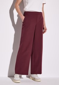Pantalon large bordeaux avec une texture lisse, taille �élastique, poches latérales et coupe ajustée, associé à des baskets blanches.
