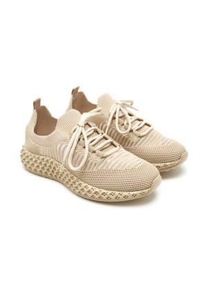 Baskets de sport beiges en tissu tricoté avec un design texturé. Elles disposent d'une semelle perforée, d'un laçage à l'avant et d'une languette au niveau du talon.