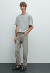 T-shirt grigio a maniche corte abbinato a pantaloni dritti grigi chiari e mocassini neri. Il tessuto appare morbido e la vestibilità è rilassata.