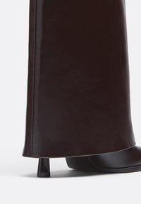 Bruna fusk läderankelstövlar med en krökt siluett och en smal klack, med en slät yta och subtil glans.
