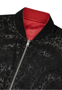 Czarna bomberka z fakturowanym wzorem w cętki, z czerwonym wnętrzem i srebrnym zamkiem błyskawicznym, podkreślona czarnym ściągaczem przy kołnierzu.