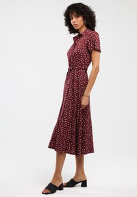 Abito midi floreale bordeaux con maniche corte, colletto, vita con cintura e gonna fluida. Indossato con sandali neri con tacco a blocco.