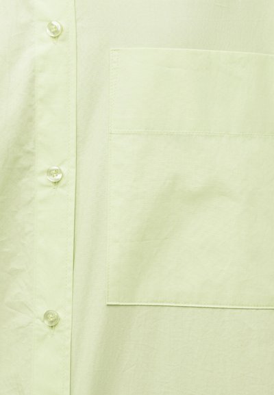 Chemise à boutons vert clair en gros plan montrant une poche avant et trois boutons translucides sur la patte de boutonnage gauche.