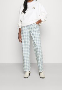 Sudadera blanca con un pequeño diseño bordado, combinada con pantalones de cuadros en tonos azul claro y crema. El modelo lleva zapatos de tacón cuadrado en color beige.