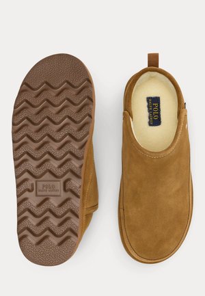 Ruskea mokkanahkainen slip-on-kenkä, jossa pehmeä, turkisvuorattu sisäpinta. Kengässä on kuvioitu kumipohja, jossa on siksak-kuvioita, ja kantapäässä lenkki helpottamaan jalkaan pukemista.