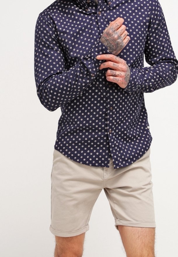 Camisa de lunares azul marino con un cierre de botones en la parte delantera y mangas largas, combinada con pantalones cortos beige claros, hechos de una tela suave.