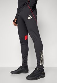 Zwarte sportbroek met rode accenten en witte strepen. Gemaakt van rekbare stof, met een elastische tailleband en zijzakken.
