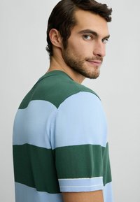 Strickoberteil mit kurzen Ärmeln und horizontalen Streifen in Grün und Hellblau. Verfügt über einen Rundhalsausschnitt und gerippte Bündchen. Weicher Stoff.