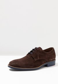 Chaussure en suède marron avec un bout rond, lacets bleus et une finition texturée. Dispose d'une semelle durable avec un accent contrastant près du talon.