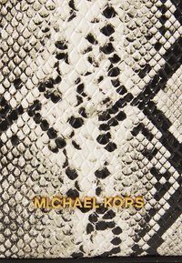 Peňaženka so vzorom hada vyrobená z textúrovanej umelohmotnej kože v čiernej a bielej farbe, s embosovanými šupinami a zlatým logom "Michael Kors".