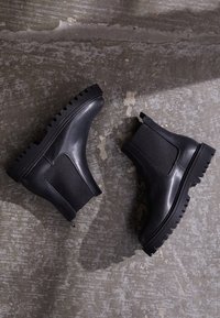 Black ankle boots with a chunky sole, elastic side panels, smooth leather finish, and a textured tread pattern on the outsole.