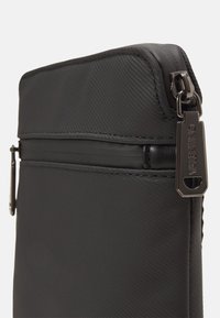 Busta nera in nylon con una texture liscia, dotata di chiusura con zip superiore e un tirazzo in metallo con marchio per un tocco di eleganza.