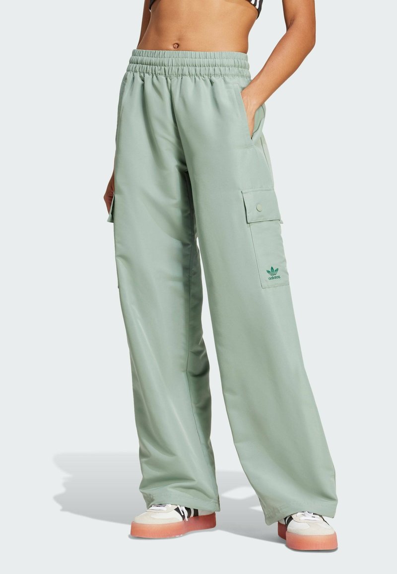 Pantaloni cargo verde chiaro con cintura elastica, tasche laterali, dettaglio con logo, vestibilità ampia e texture morbida, abbinati a sneakers multicolori.