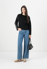 Black knit sweater with white accent stitching at shoulders, paired with light blue wide-leg jeans and animal print sneakers. Black handbag.