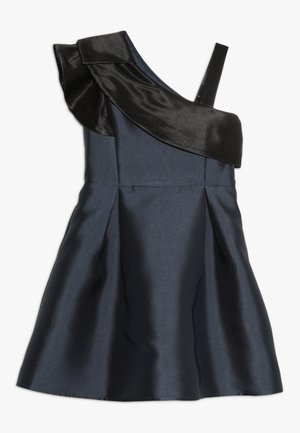 Granatowa sukienka bez rękawów z jednym czarnym, opadającym na ramię falbanką i asymetrycznym, pojedynczym paskiem po prawej stronie.