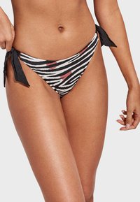 Parte inferior de bikini a rayas blancas y negras con acentos rojos, con detalles de lazo a los lados y una textura de tela suave, diseñada para un ajuste ceñido.