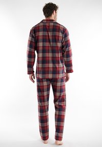Flanellen pyjama set met een geruiten patroon in rood, marineblauw en crème. Bevat een blouse met kraag en bijpassende broek, en heeft een ontspannen pasvorm.