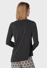 Svart långärmad skjorta med rundad halsringning och avslappnad passform, med en något förlängd bakre fåll. Bärs med mönstrade byxor.