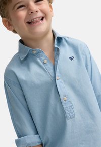 Camisa de botón azul claro hecha de una tela suave, con cuello, mangas largas y un pequeño logo en navy en el pecho.
