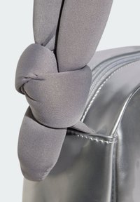 Gray fabric knot accent on a shiny metallic silver shoulder bag, featuring a smooth texture, rounded shape, and contrasting stitching detail.