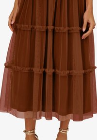 Braunes, schichtweise gestaltetes Midikleid aus transparenter Stoff, mit Rüschendetails und gefüttertem Rock. Es hat vertikale Streifen und eine fließende Silhouette.
