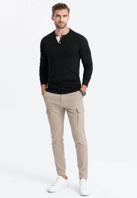 Schwarzes Langarm-Henley-Shirt mit knopflosem Ausschnitt, kombiniert mit hellbeigen Cargo-Hosen und weißen Sneakern. Glattes Material, taillierte Passform.