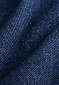 Tela de mezclilla en un azul profundo con una superficie suave y texturizada. Presenta un sutil patrón de tejido y ligeras variaciones en la intensidad del color.
