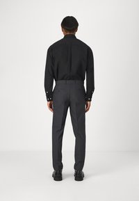 Svart långärmad skjorta med knapppdetaljer, matchad med grå skräddarsydda byxor. Outfiten har en figurnära design och subtila texturer.