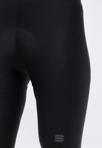 Κοντινό πλάνο μαύρου επενδυμένου σορτς ποδηλασίας που δείχνει τις λεπτομέρειες των ραφών και το αντανακλαστικό λογότυπο στο μηρό.