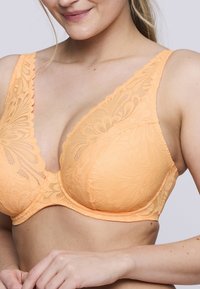 Sujetador de encaje en suave naranja con patrón floral, escote pronunciado, tirantes anchos y tejido texturizado. Presenta copas lisas y moldeadas con bordes ondulados.