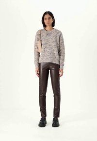 Világosszürke kötött pulóver texturált mintával, sötétbarna bőrnadrággal és fekete platform cipővel párosítva; a modellen egy bézs táska van.