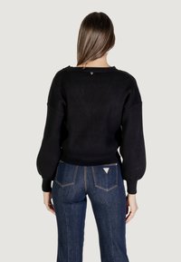 Maglione nero a coste con vestibilità rilassata, caratterizzato da maniche a palloncino e un leggero scollo a barca. Abbinato a jeans a vita alta.