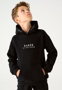 Must kapuutsiga dressipluus esitaskuga, millel on valged tähed "BAKER BY TED BAKER." Pehme kangas, mugav lõige, soonikkoes mansetid.