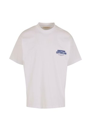 Bílý bavlněný tričko s kulatým výstřihem a krátkými rukávy. Na přední straně se nachází modrý potisk s textem "ANOTHER COTTON LAB".