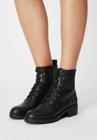 Black ankle boots made of textured leather with laces and metal eyelets, featuring a block heel and rugged outsole for traction.