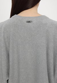 Maglione grigio a maglia con scollatura rotonda. Un piccolo logo MK argentato è visibile sul retro. Tessuto liscio e testurizzato con finitura a coste.