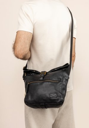 Black leather shoulder bag with a textured surface, a zippered front pocket, and bronze hardware accents. Adjustable fabric strap.
