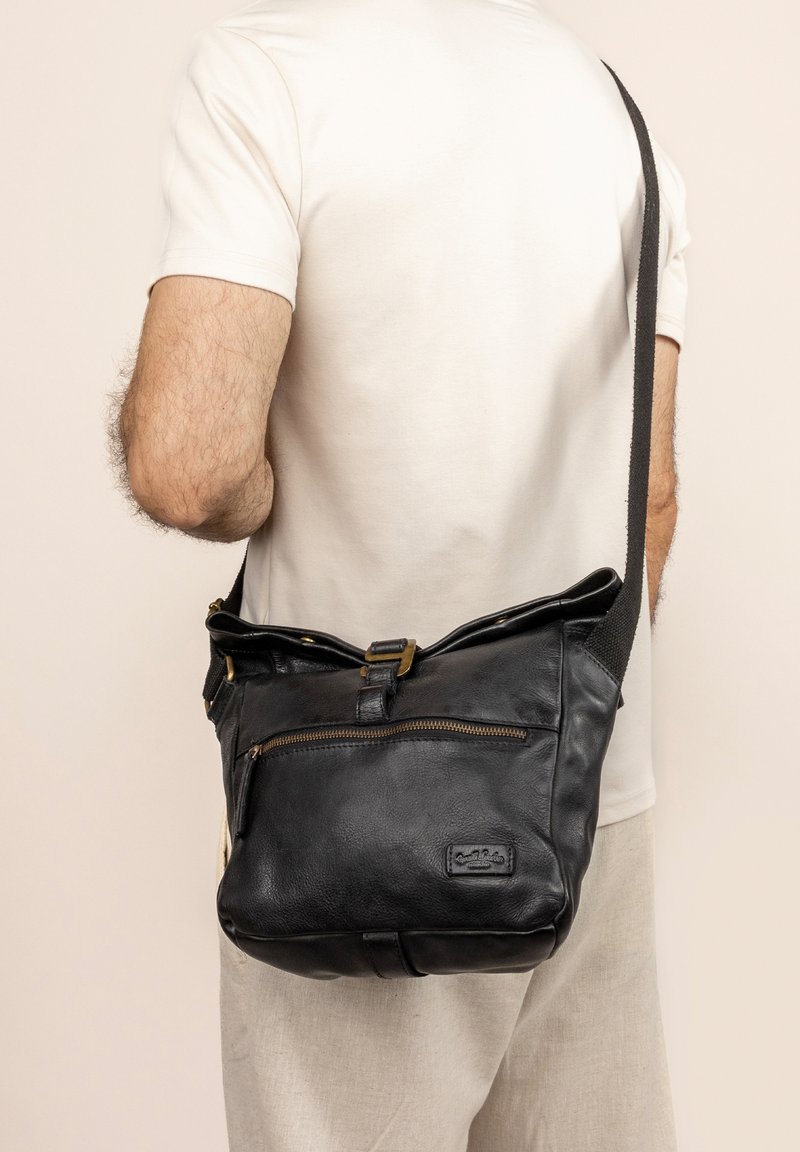 Black leather shoulder bag with a textured surface, a zippered front pocket, and bronze hardware accents. Adjustable fabric strap.