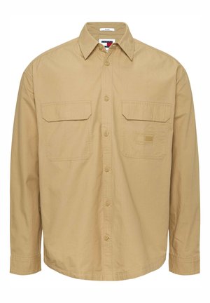 Chemise beige à manches longues avec boutons, deux poches poitrine et un petit logo brodé sur la poche gauche.