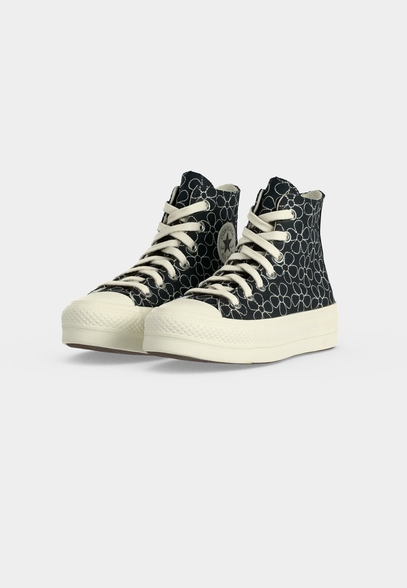 Schwarze High-Top-Sneaker mit weißem Blumen-Umrissmuster, weißen Gummisohlen und weißen Schnürsenkeln auf schlichtem hellem Hintergrund.