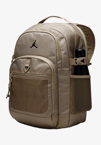 Beiger Rucksack mit strukturierter Oberfläche, ausgestattet mit einer Fronttasche, einer Netztasche an der Seite, Reißverschlussverschlüssen und einem schwarzen Logo. Inklusive Flaschenhalter.