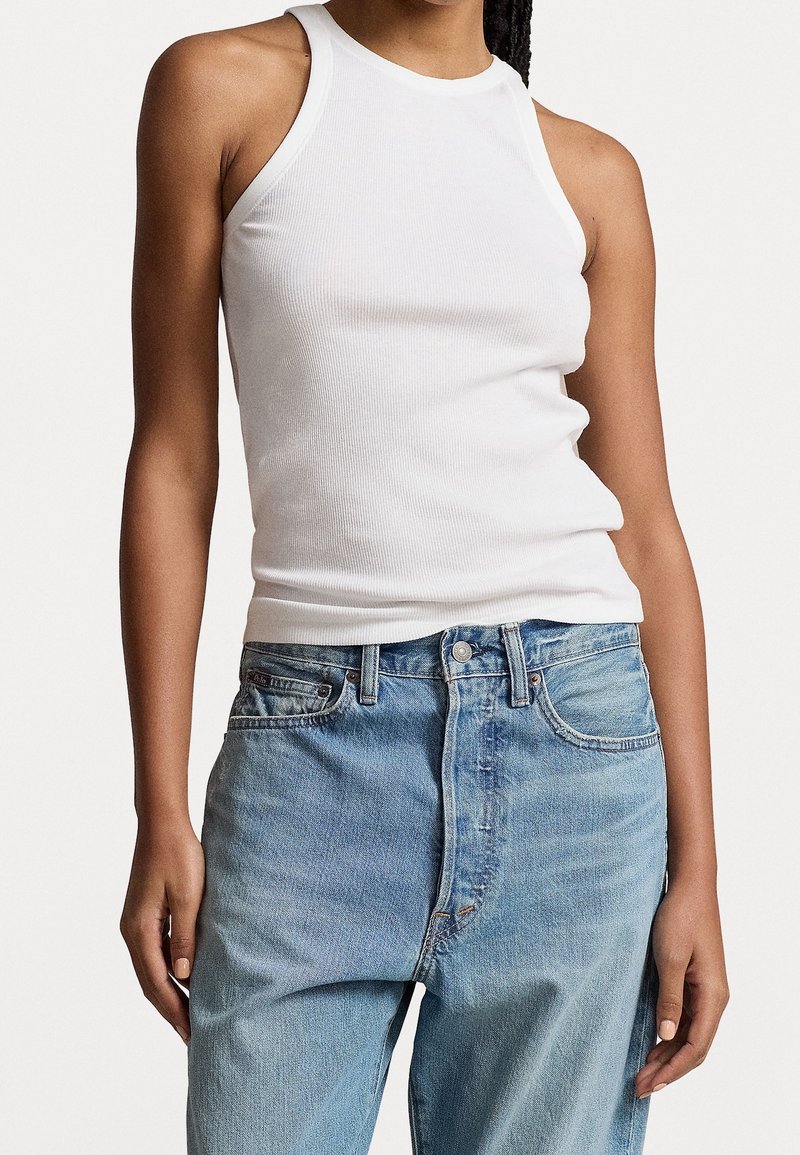 Bílý žebrovaný halter top se přiléhavým střihem, spárován se světle modrými jeansy s vysokým pasem, které mají knoflíkový zapínání a jemné blečení.