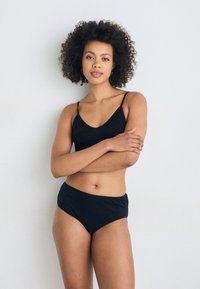 Zwart geribbelde bralette en high-waisted slipset. De bralette heeft dunne bandjes en een v-hals ontwerp. Gladde textuur overal.