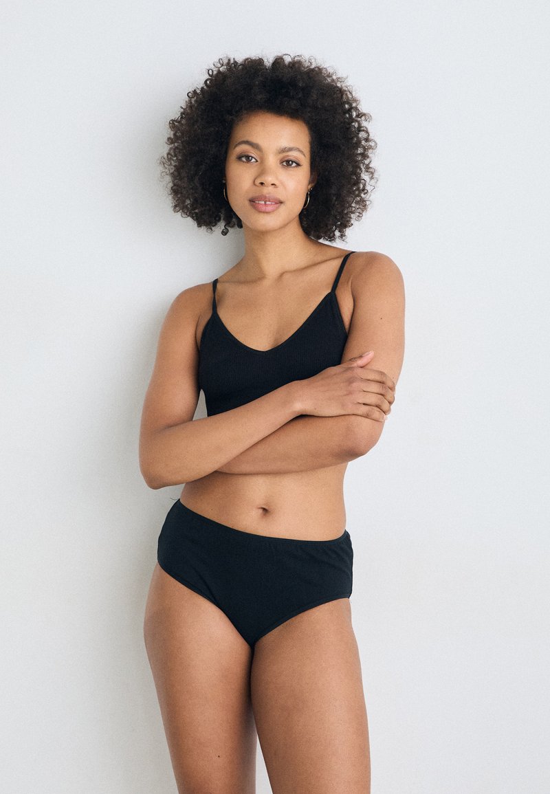 Zwart geribbelde bralette en high-waisted slipset. De bralette heeft dunne bandjes en een v-hals ontwerp. Gladde textuur overal.