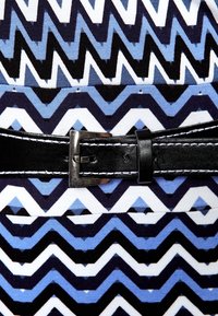 Sukienka w wzory z zygzakowymi paskami w odcieniach niebieskiego, czarnego i białego, uzupełniona czarnym paskiem ze srebrną klamrą.